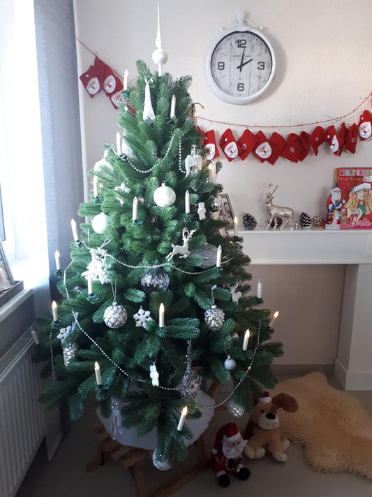 Geschmückte künstliche Douglasie mit silbernen Kugeln und Lichterkette im Wohnzimmer