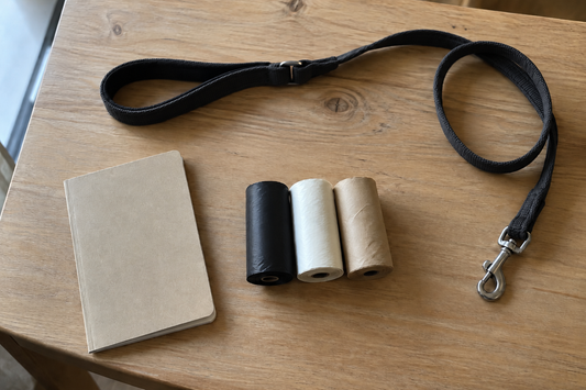 Drei Rollen Hundekotbeutel in Schwarz, Weiß und Beige neben Leine und Notizbuch (KI-generiertes Bild)