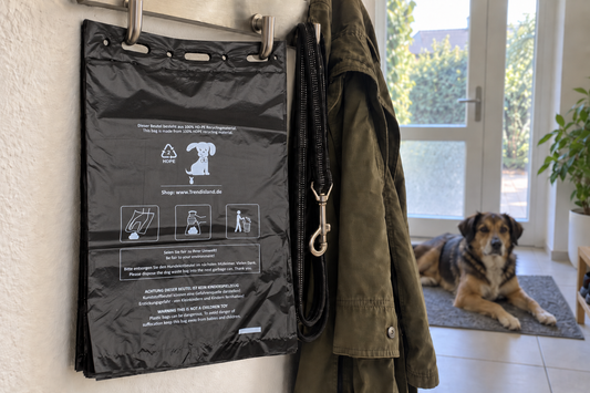 1000 schwarze Hundekotbeutel im Block an zwei Garderobenhaken im Flur, daneben Leine und Jacke, Hund auf der Fußmatte (KI-generiertes Bild)